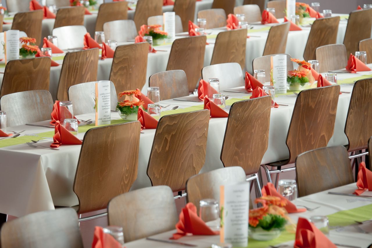 who-we-are Beautifully arranged tables with wooden chairs for a formal event, adorned with orange flowers.
